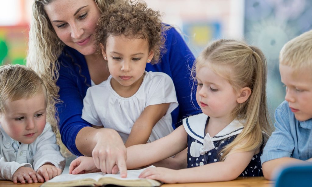 An adult and four children sitting around a table in a Sunday School classroom, reading a Bible, in an article about Lent Activities for Kids