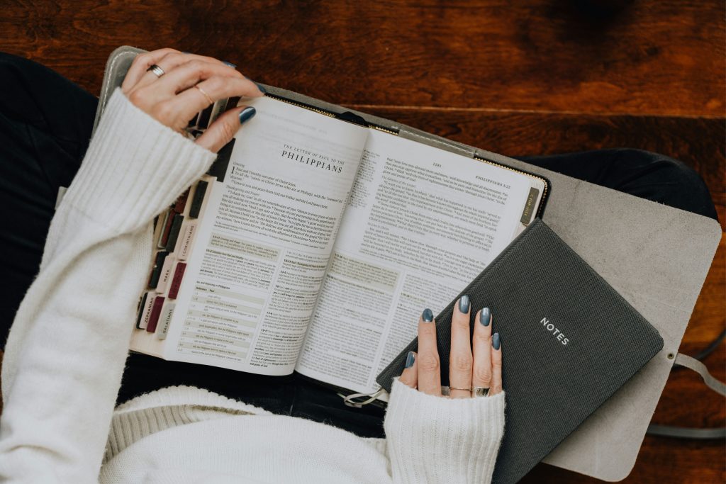 woman with painted nails reading a passage from the Bible and holding a notebook